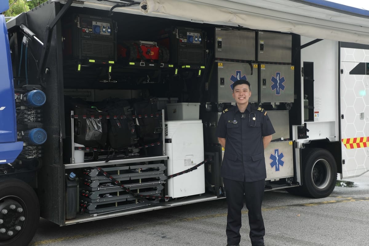 Medic in navy uniform stands before open ambulance truck filled with Honda generators and medical equipment.