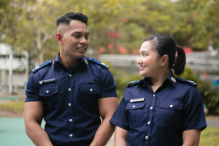Two Singaporean police officers in uniform looking at each other outside.