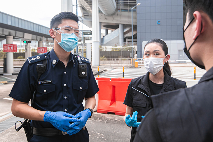 Two people with face masks and gloves speak to a Singapore police officer wearing similar protection.