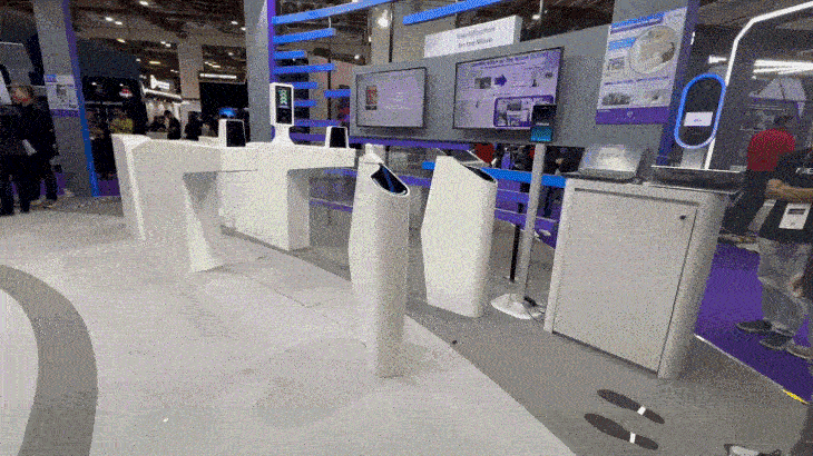 Exhibition booth with screens, white counters and kiosks, displaying interactive technology.