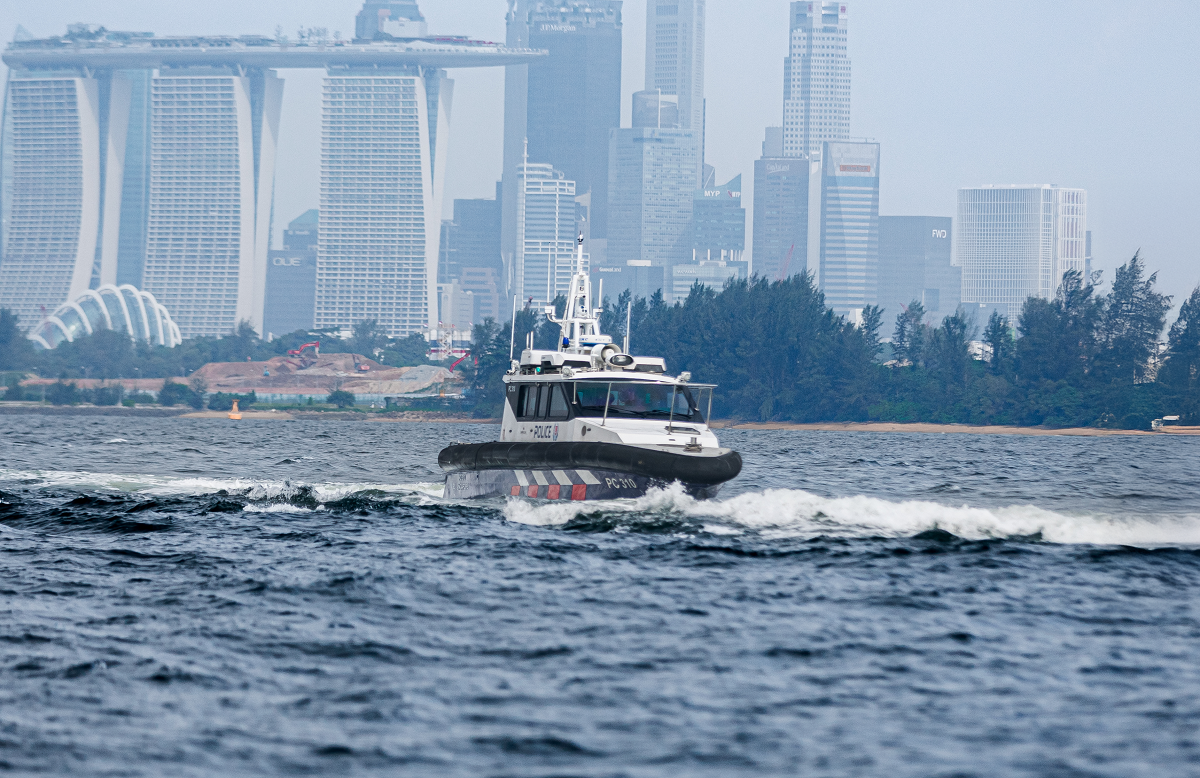 Singapore Police boat moving on water, skyscrapers including Marina Bay Sands in background.