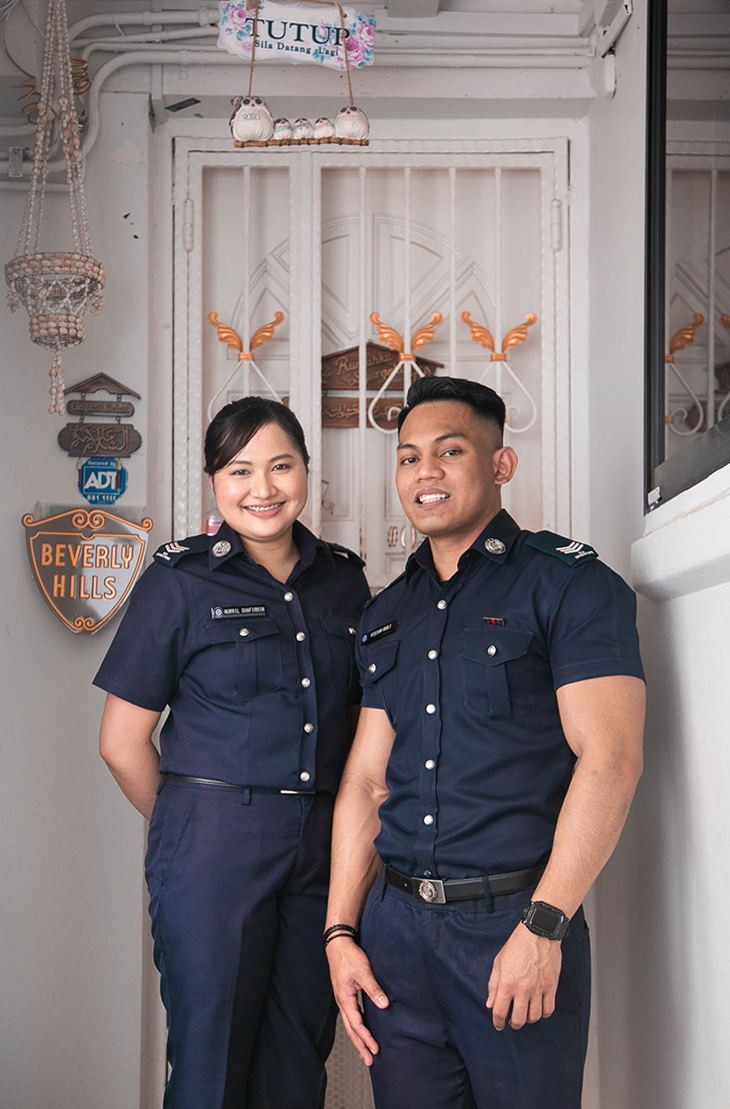 Two officers in navy uniforms pose in front of a white door.