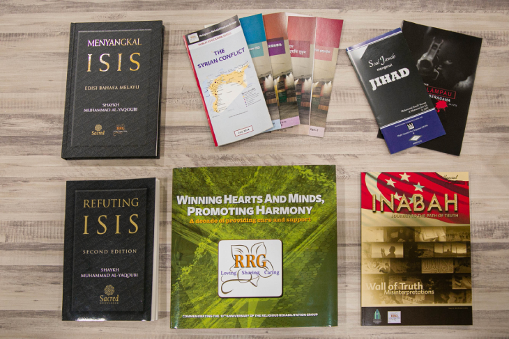 Books and pamphlets on a wooden surface, titles include "ISIS", "Jihad" and "Syrian Conflict".