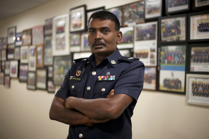 Man in police uniform with arms crossed stands before a wall of framed photos.