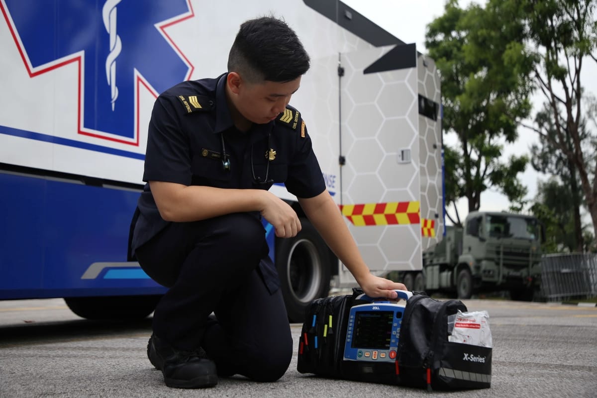 Medic in uniform kneels by a Zoll X-Series monitor with ambulance featuring a blue Star of Life symbol behind.