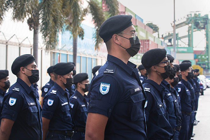A line of Civil Defence Force members in uniform, black berets, and masks stands at attention.