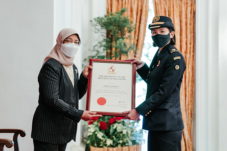 Two masked women hold a framed certificate from The President of the Republic of Singapore.