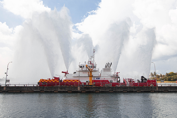 SCDF fireboat spraying large water jets from the deck while docked.