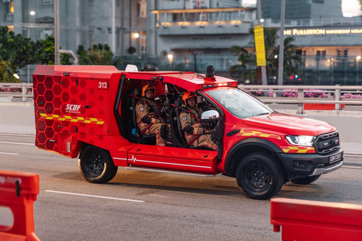 Red SCDF rescue vehicle, a modified Ford Ranger, with two uniformed firefighters inside.