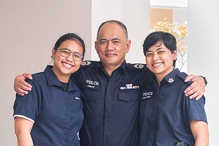 Three people in POLCE uniforms smile, arms around each other. "Police" patch visible.