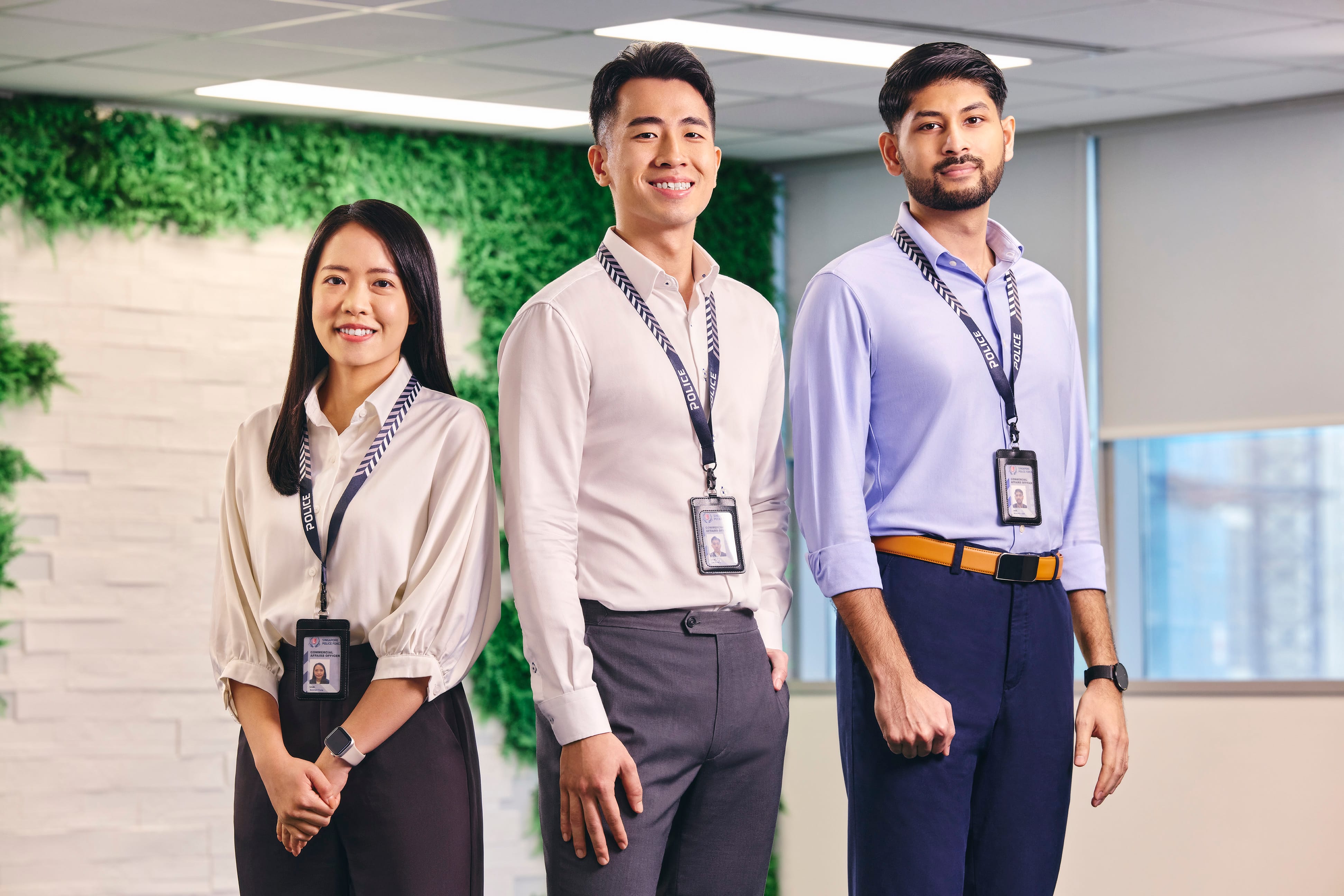 Three Commercial Affairs officers standing and smiling