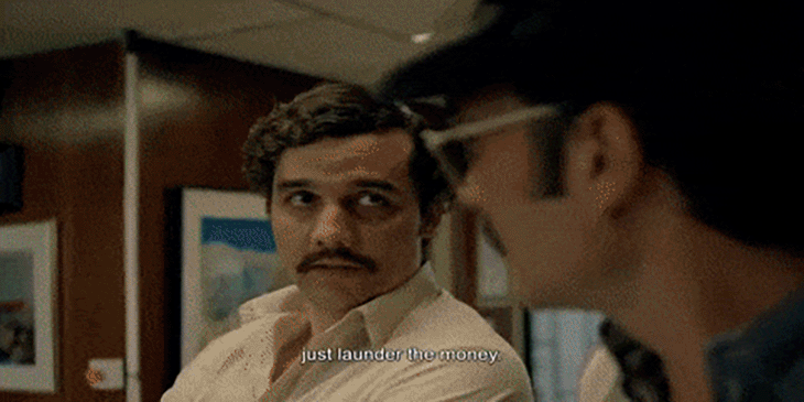 Man with mustache, likely Pablo Escobar from "Narcos," speaking to another man. Subtitles read "Just launder the money."