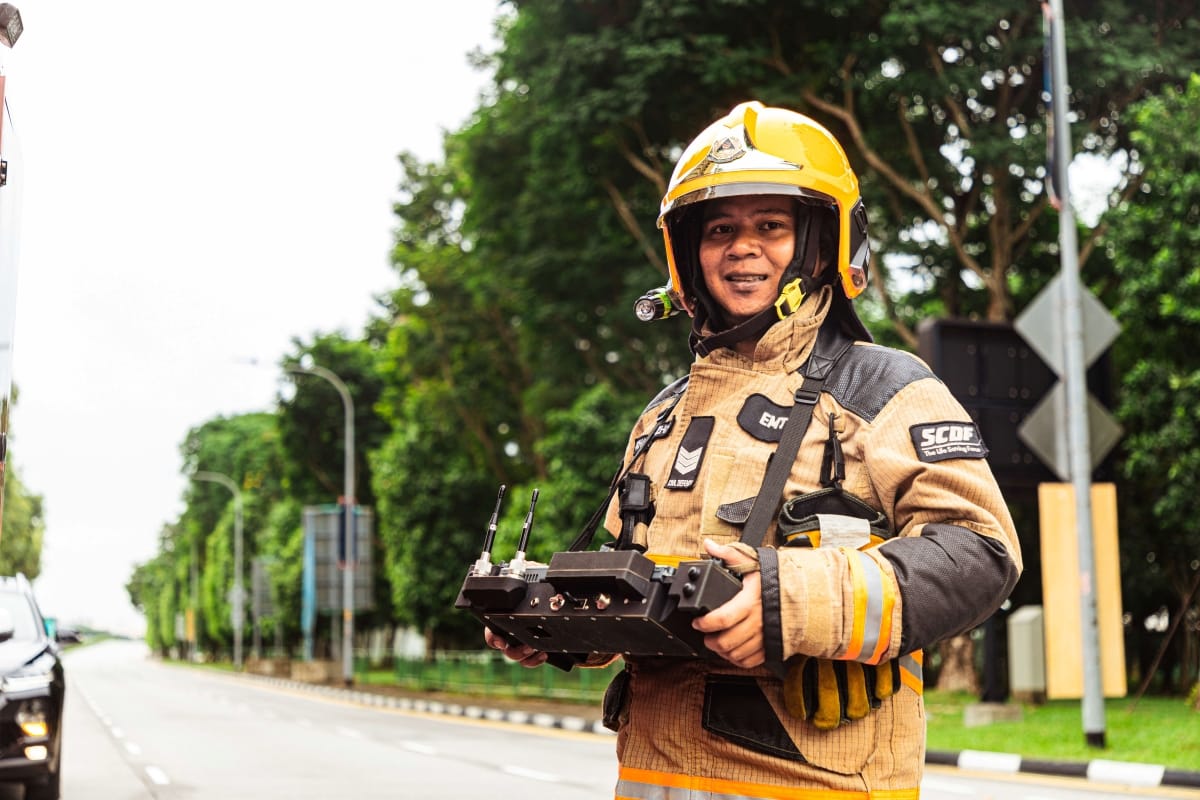 Firefighter in SCDF uniform, wearing a helmet, holding a remote control on a road.
