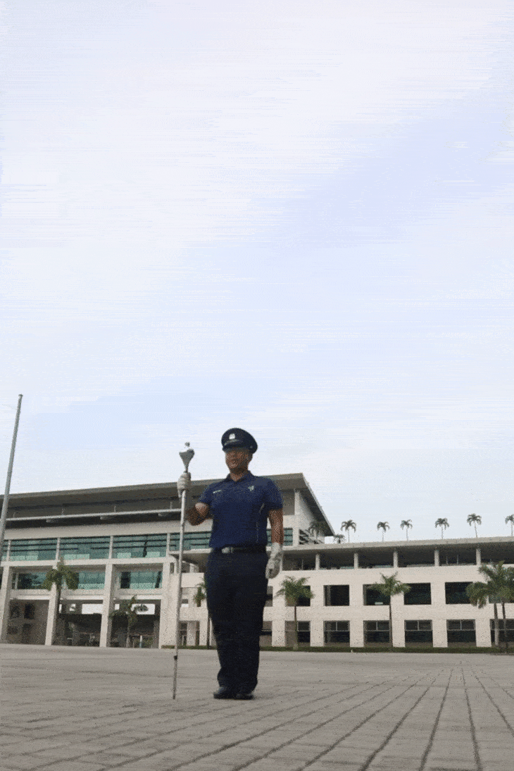 Person in uniform holding baton standing in front of building.