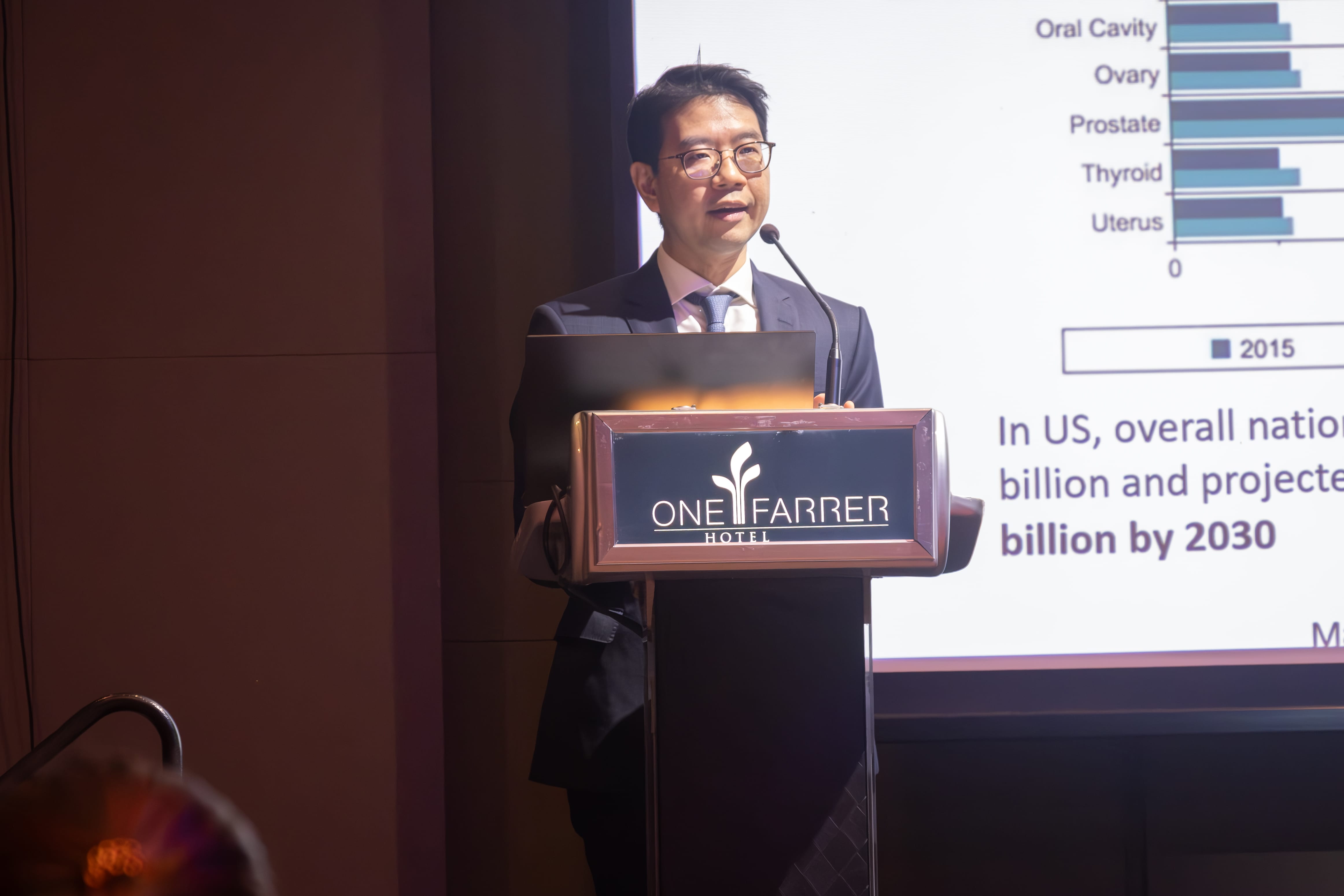 Photograph shows A/Prof Daniel S. W. Tan standing at a lectern on a stage during the NMRC awards ceremony and research symposium.