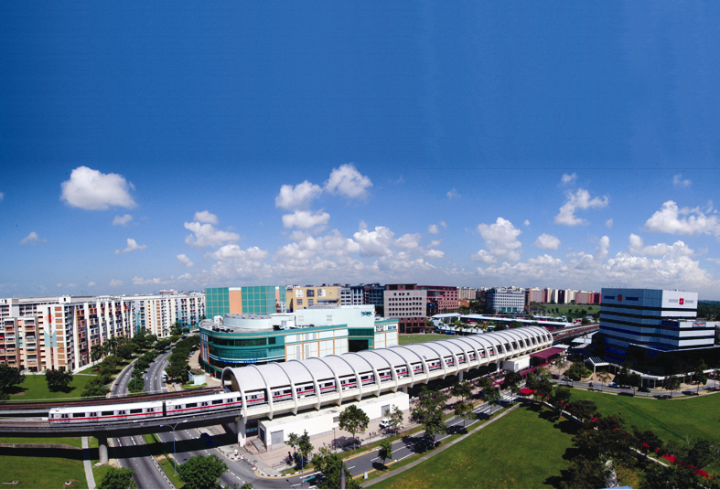 Aerial view of a cityscape with buildings, a covered train station, a moving train, and a bright blue sky with scattered clouds.