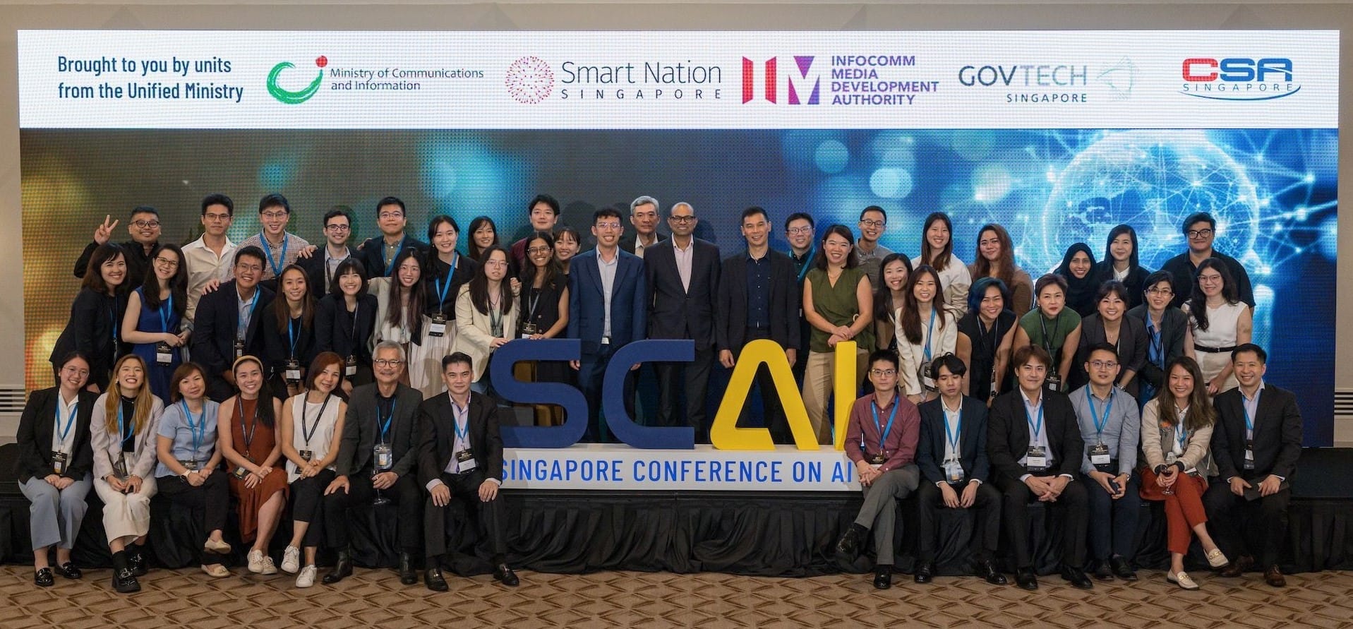 A large group photo at the Singapore Conference on AI, in front of a screen with various organization logos.