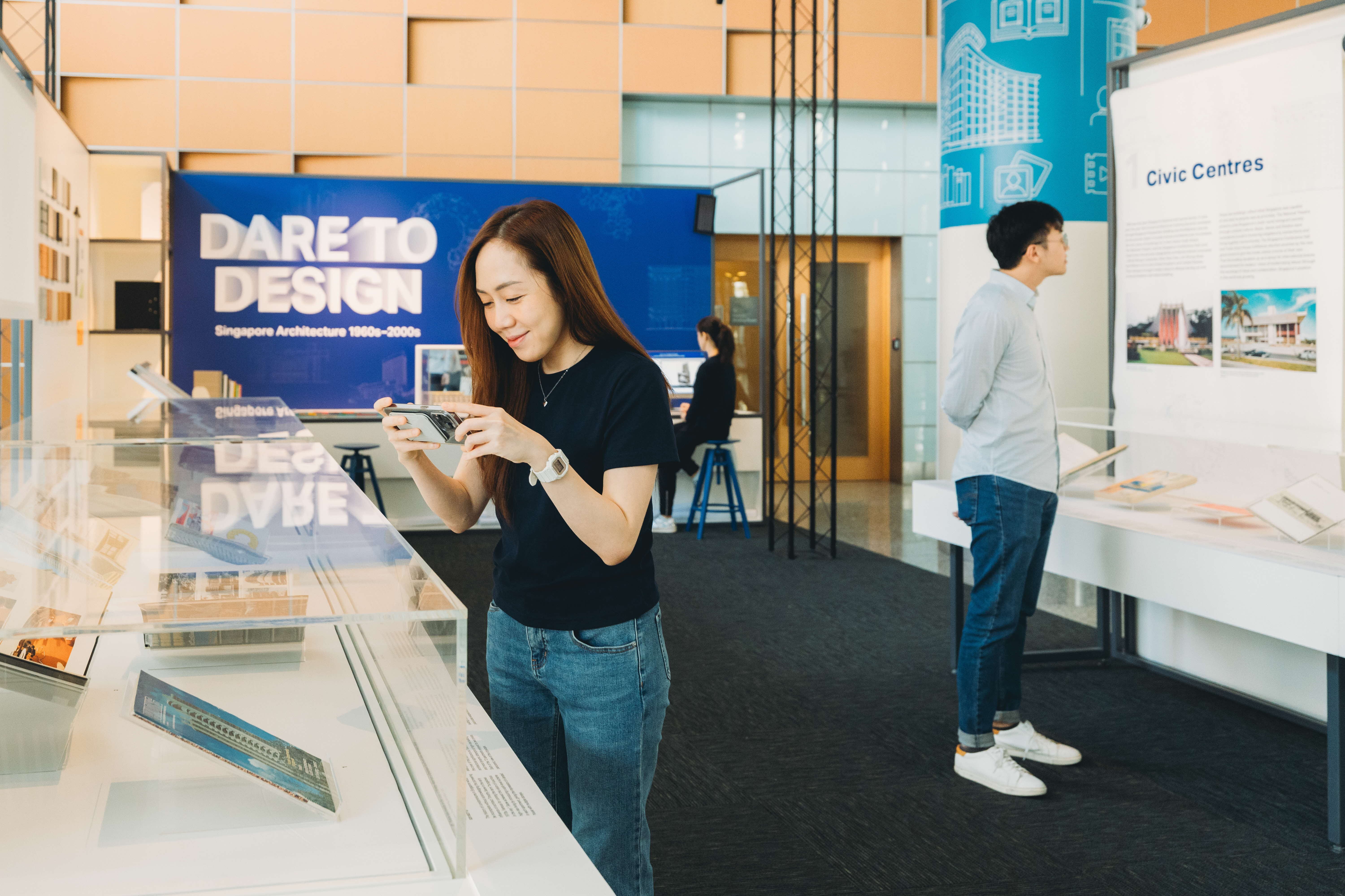 People observing exhibits in a design museum, with posters and display cases around them.