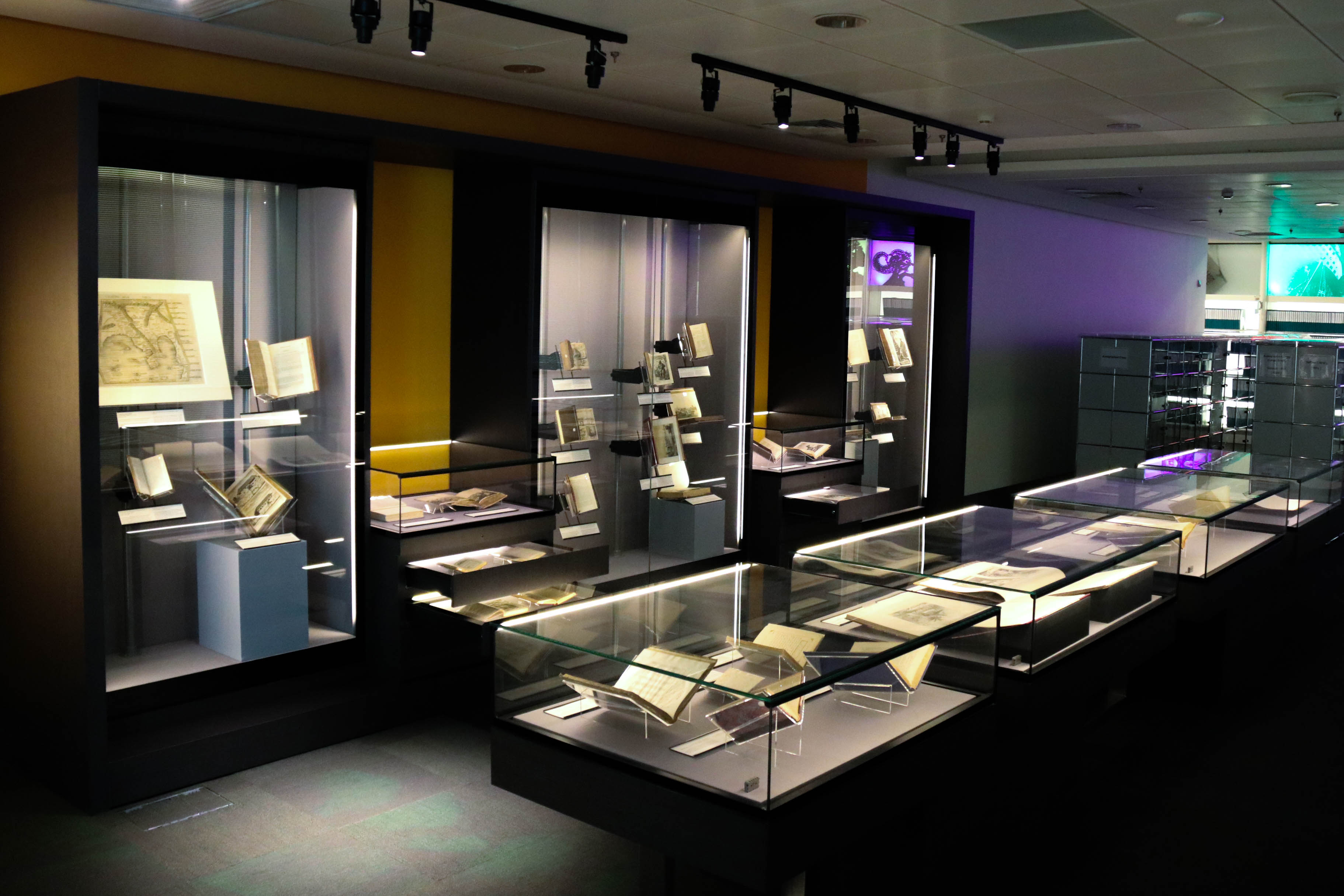 A museum exhibit displays various old books and manuscripts in glass cases and on shelves.