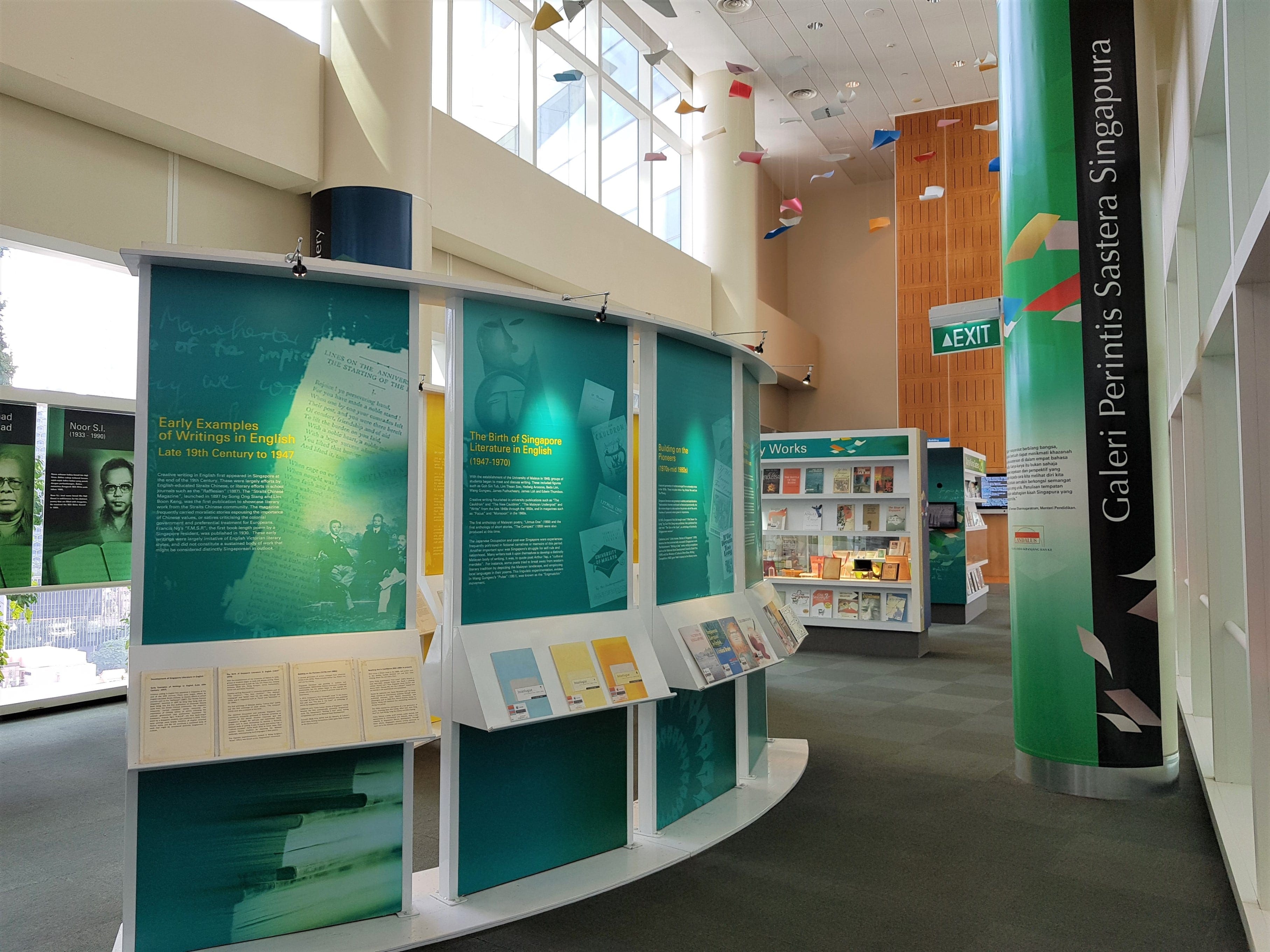 A modern gallery with informational displays, books, and a large cylinder labeled "Galeri Penulis Sastera Singapura."