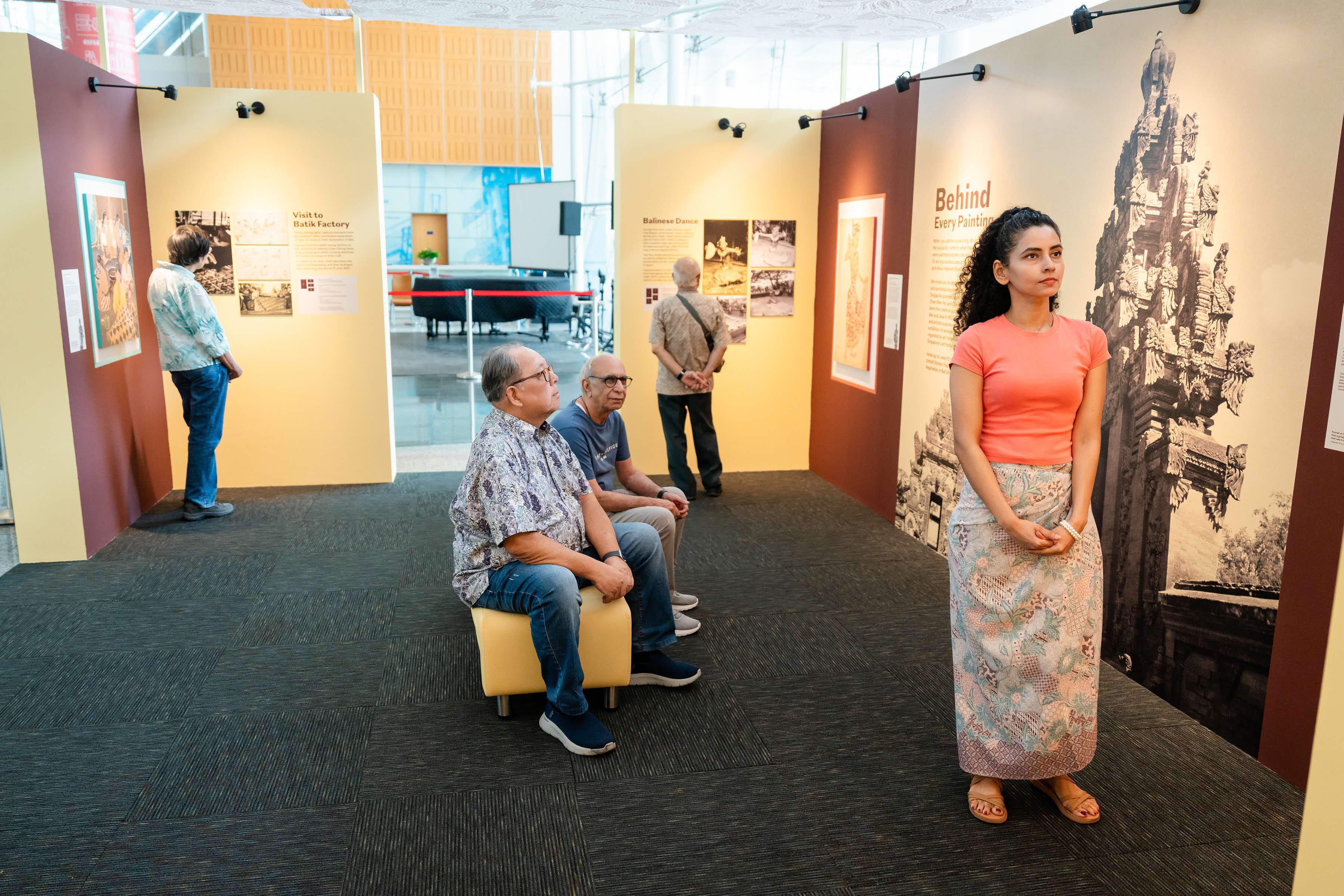 An exhibition space with four people looking at displayed photographic prints and descriptions on the walls.