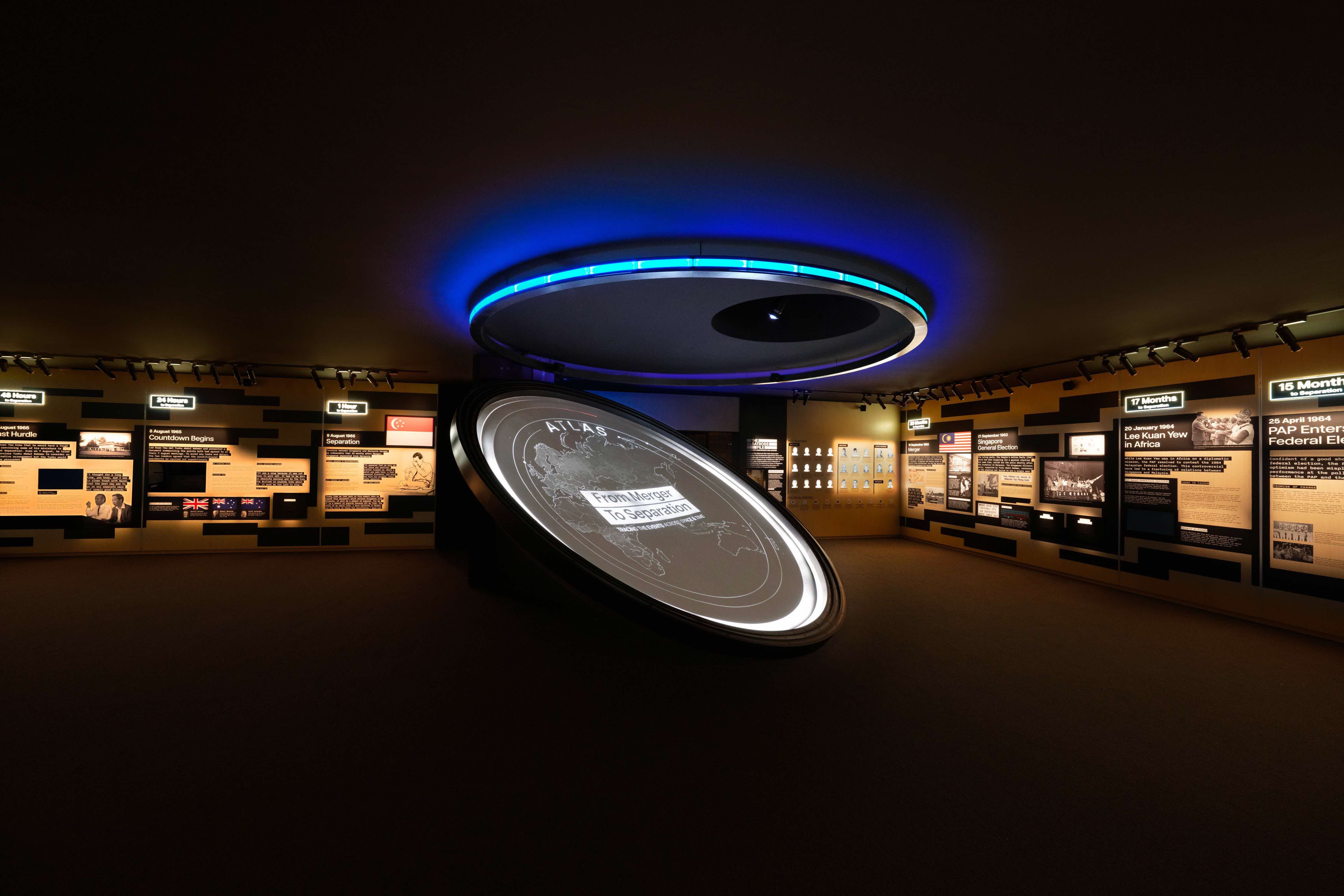 A dimly lit museum exhibit with information panels on the walls and a large circular display table in the center.