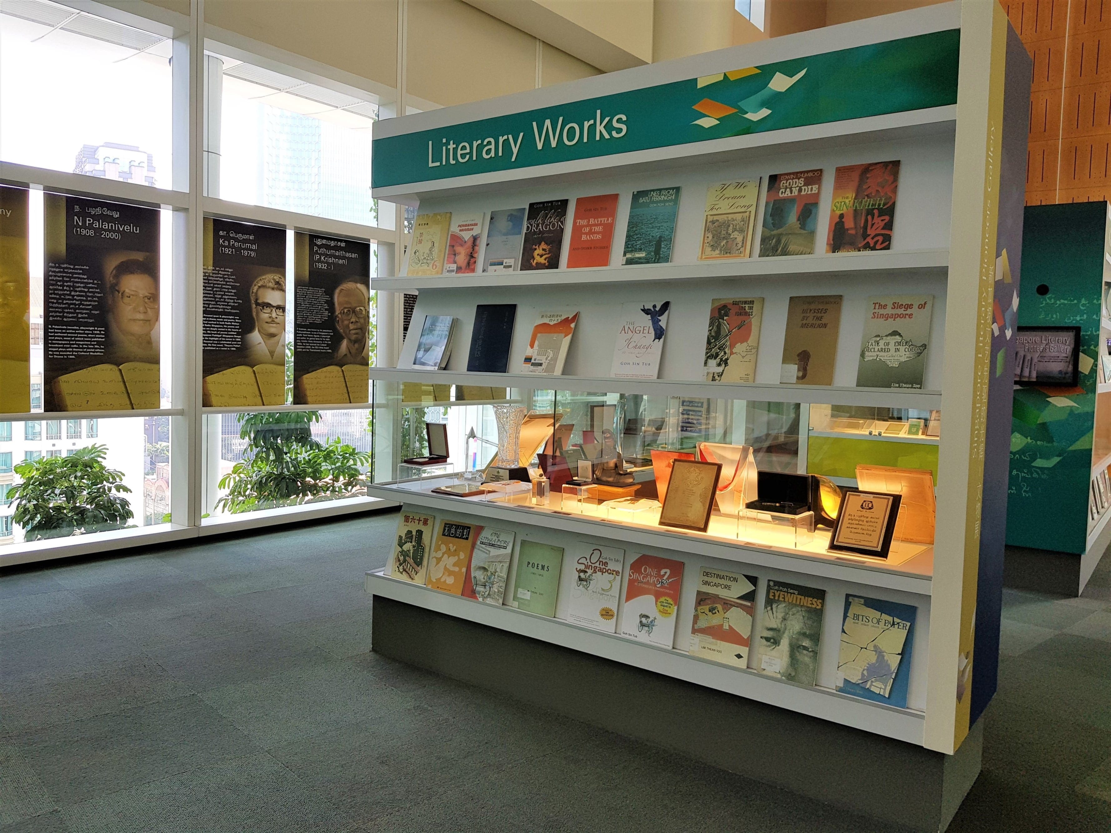 A display shelf labeled "Literary Works" features a variety of books and framed items in a room with large windows.