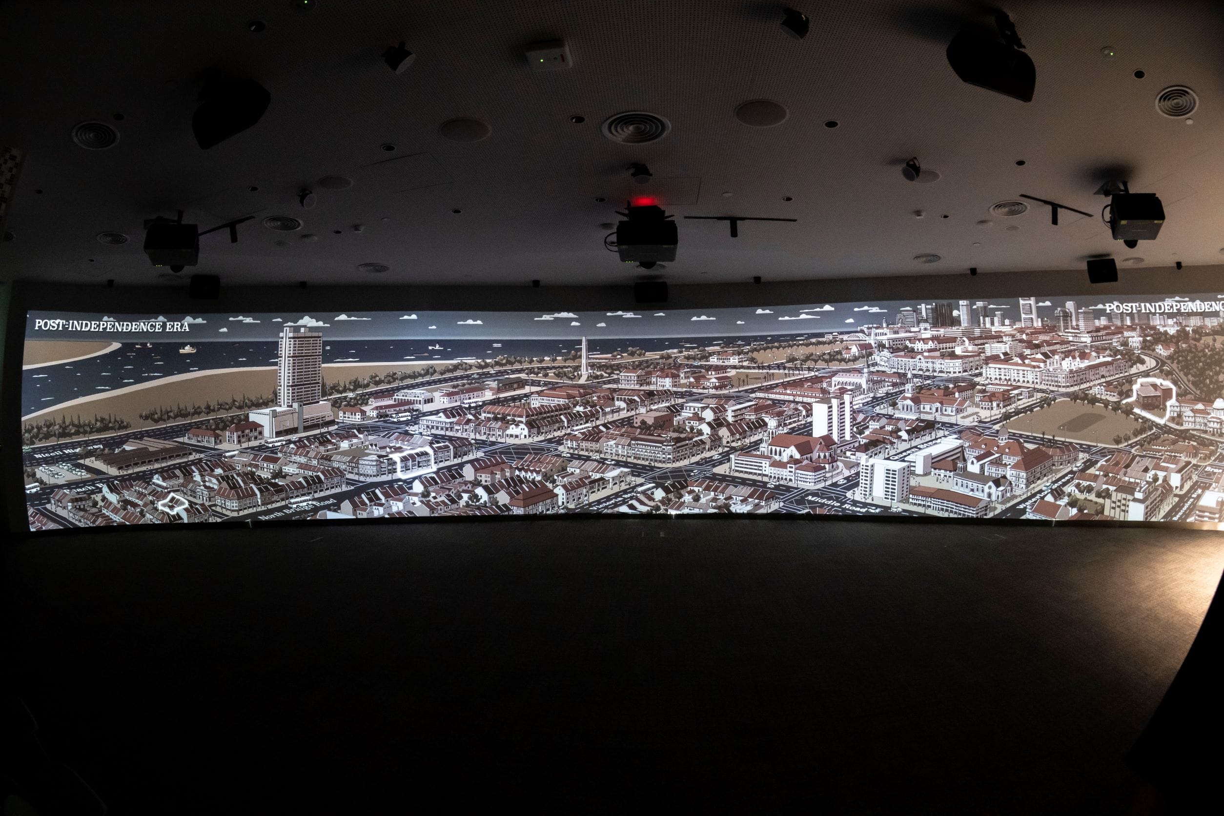 A panoramic cityscape mural labeled "Post-Independence Era" is projected on a large wall inside a dark room.