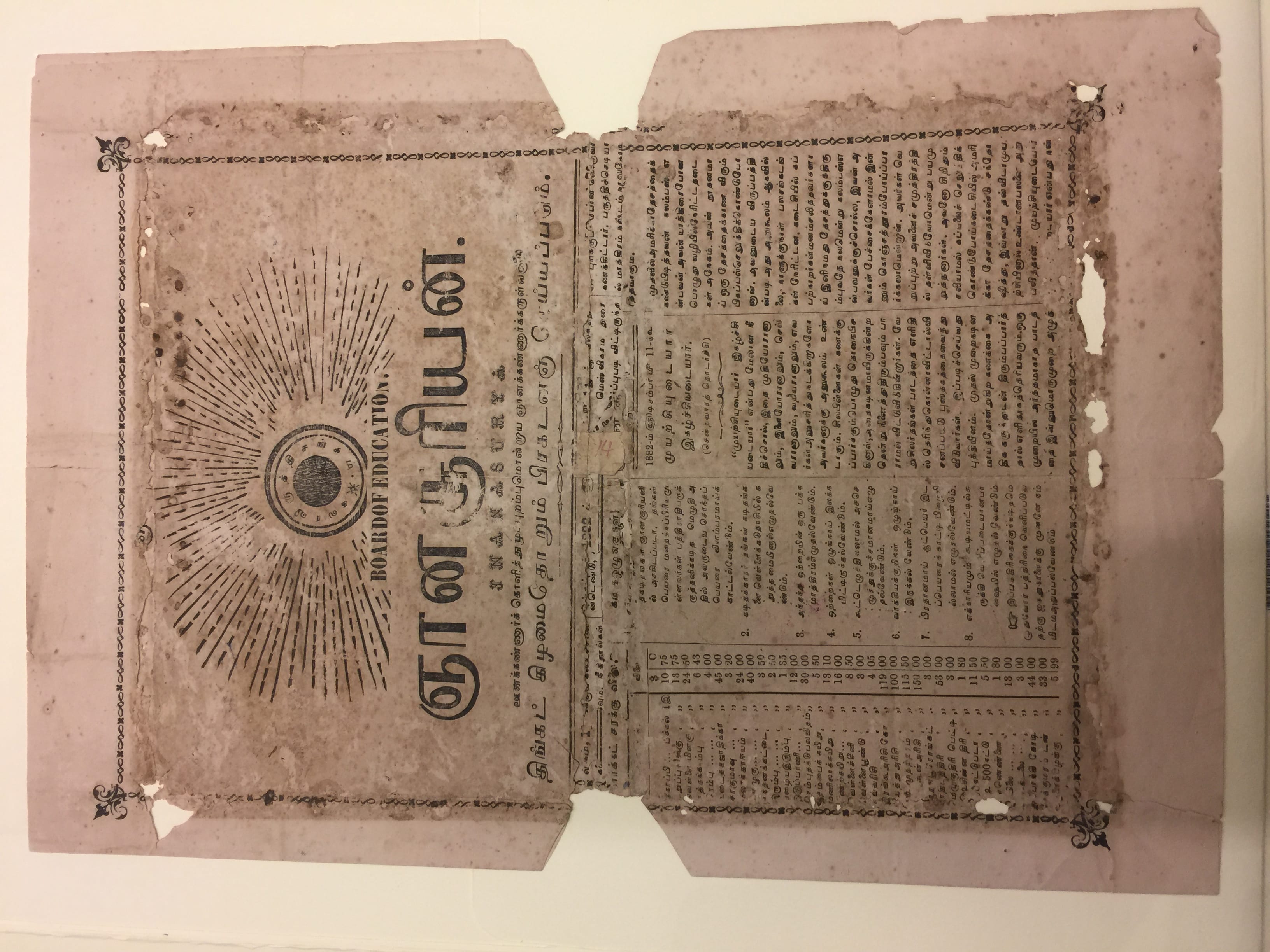 An old document with Tamil script, a decorative border, and a circular emblem with radiating lines at the top left.