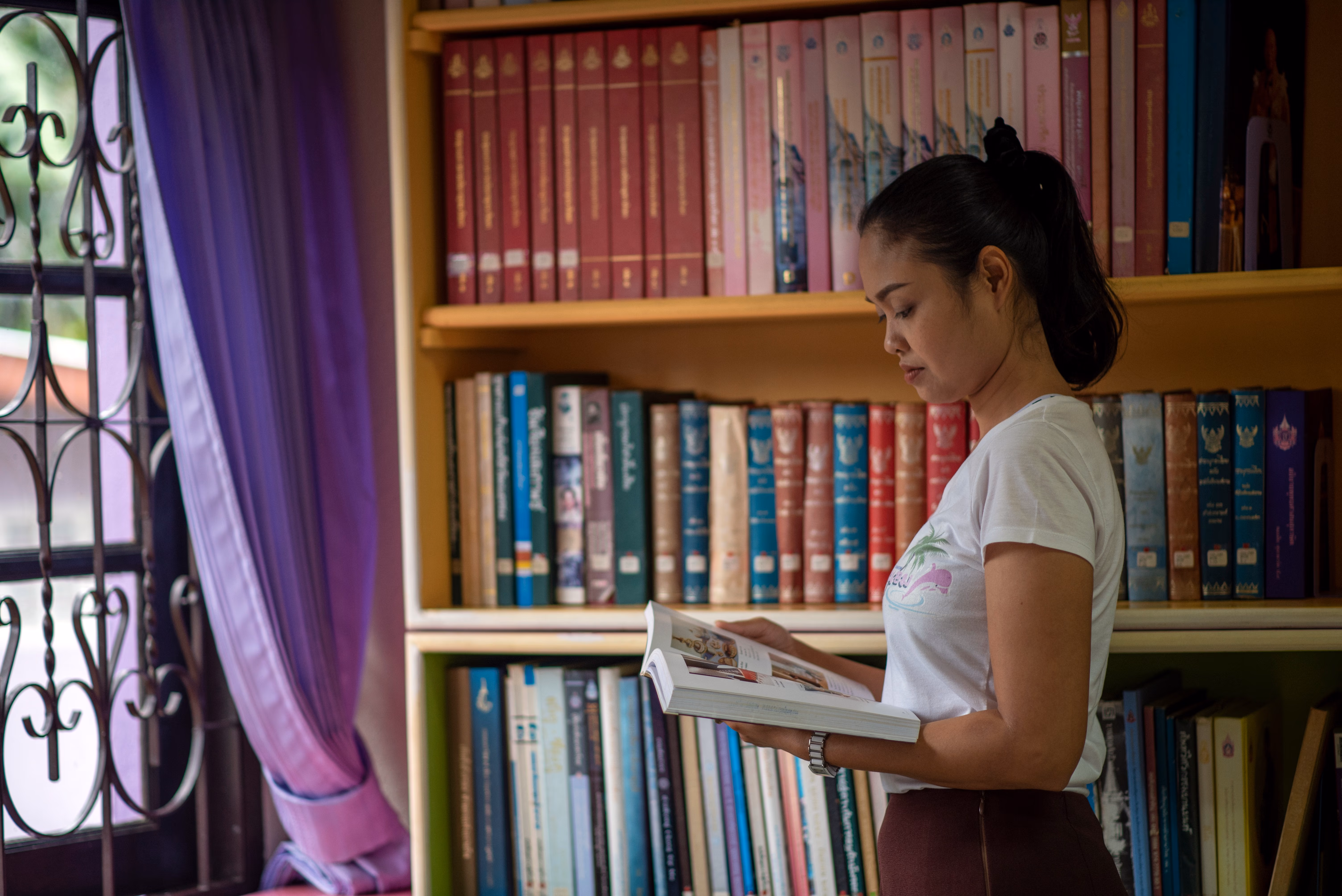Woman enjoying a quiet moment reading by a window in a cozy library setting