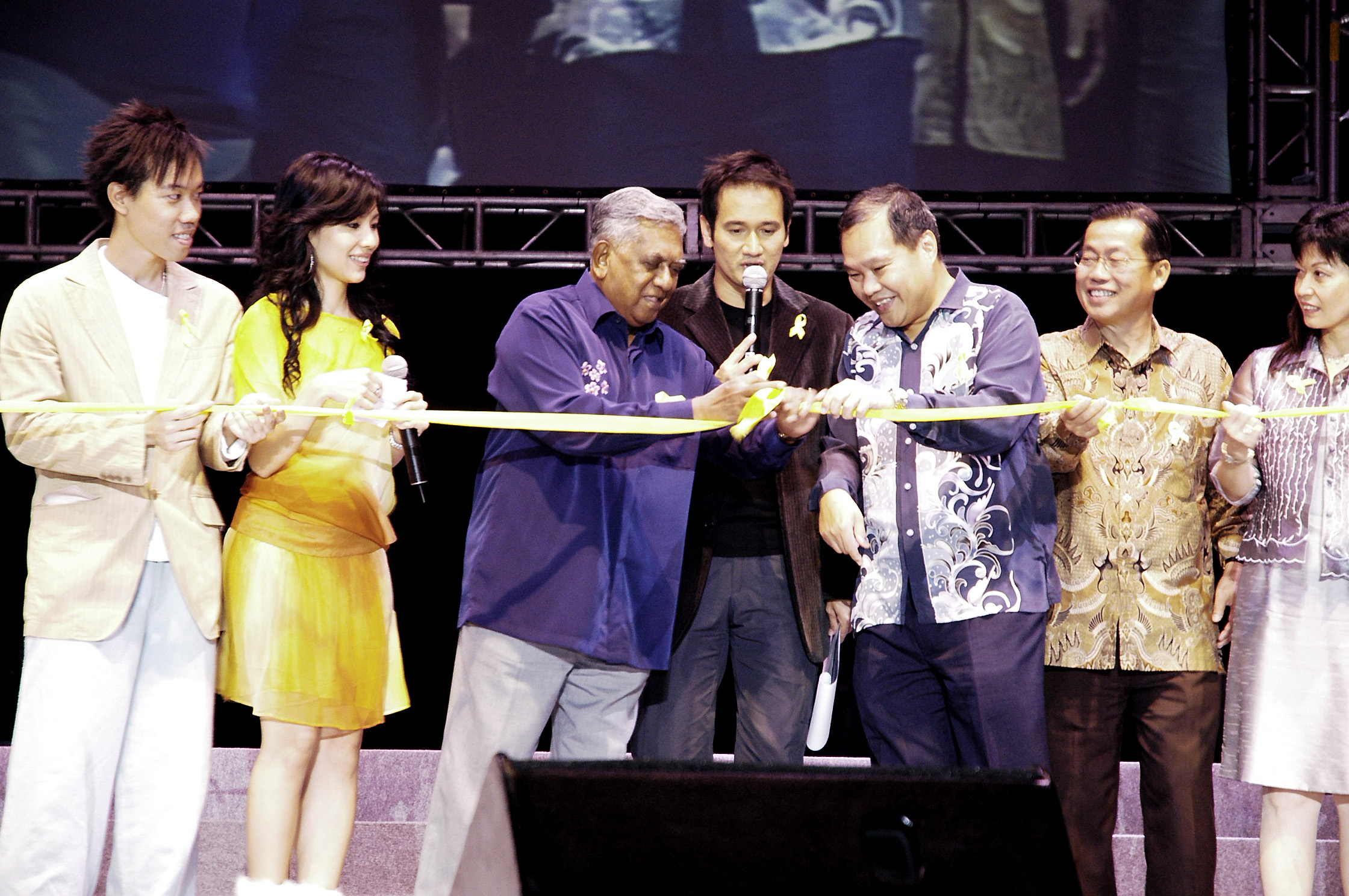Seven people stand in a row cutting a ribbon at a ceremony.