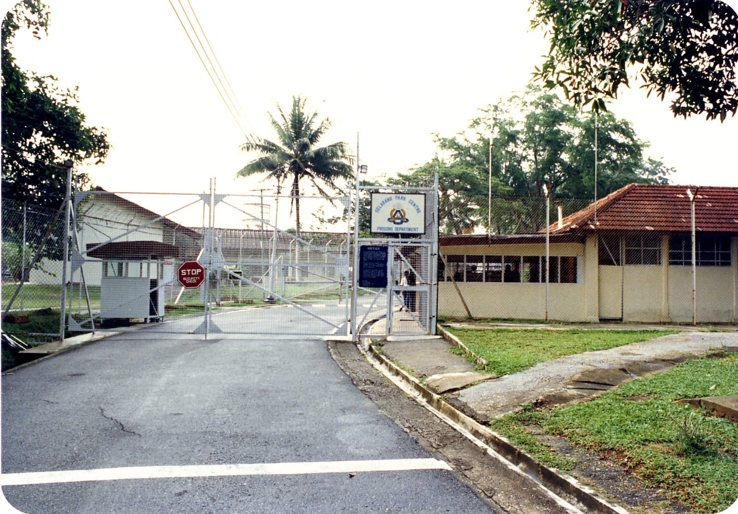 A fenced facility entrance with a stop sign, guard booth, and a sign reading "Changi Park Centre, Prisons Department."
