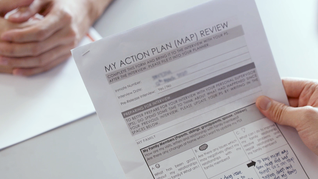 A hand holding a document titled "My Action Plan (MAP) Review," next to another person's folded hands.