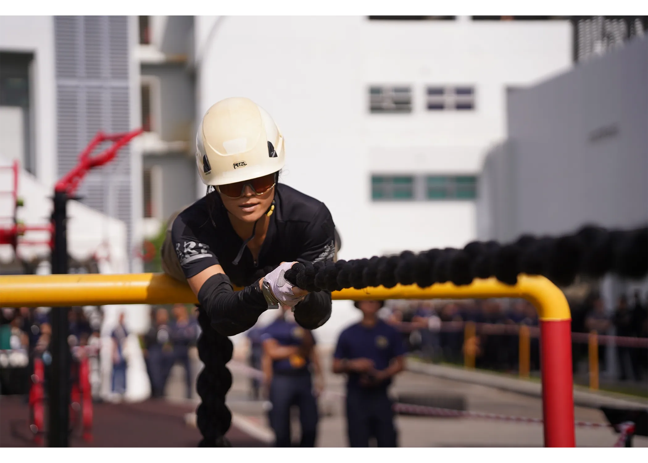 A female officer traversing the commando rope event (an event where challenger has to traverse across a thick rope that is hanging across two structure, similar to a tight rope)