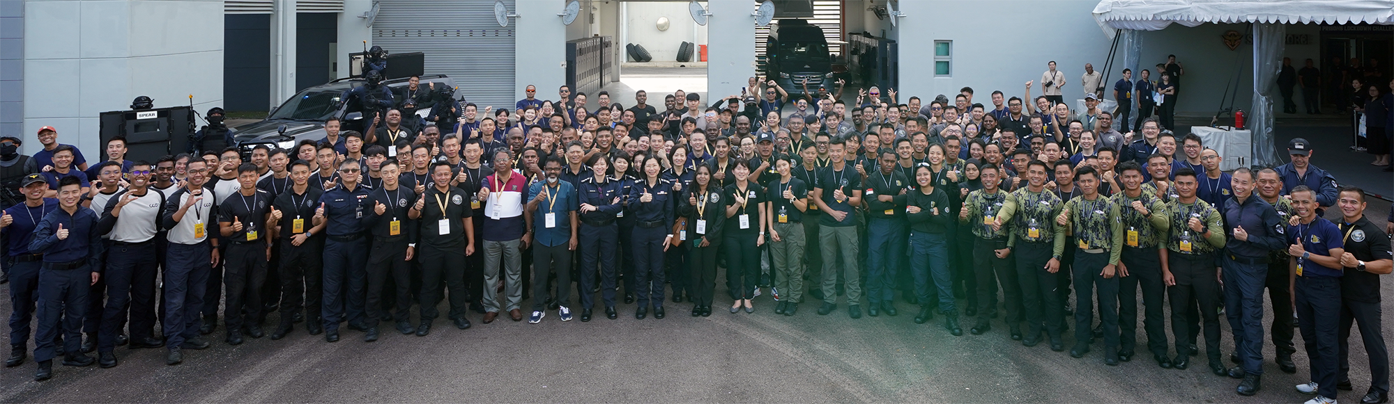A large group of people in uniform standing together outside next to a building and two vehicles.