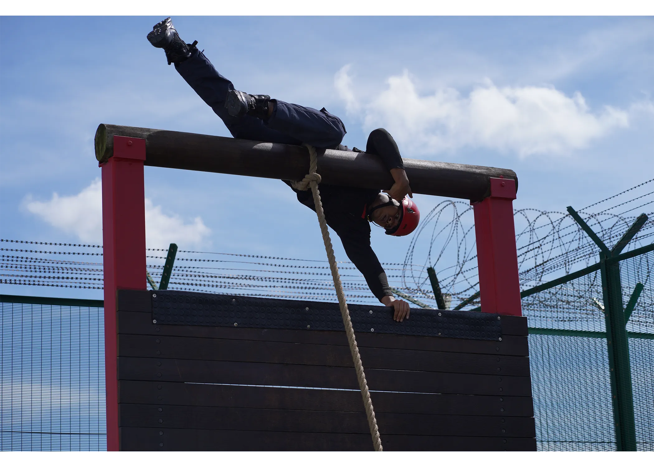 An officer climbing over the rope wall obstacle course