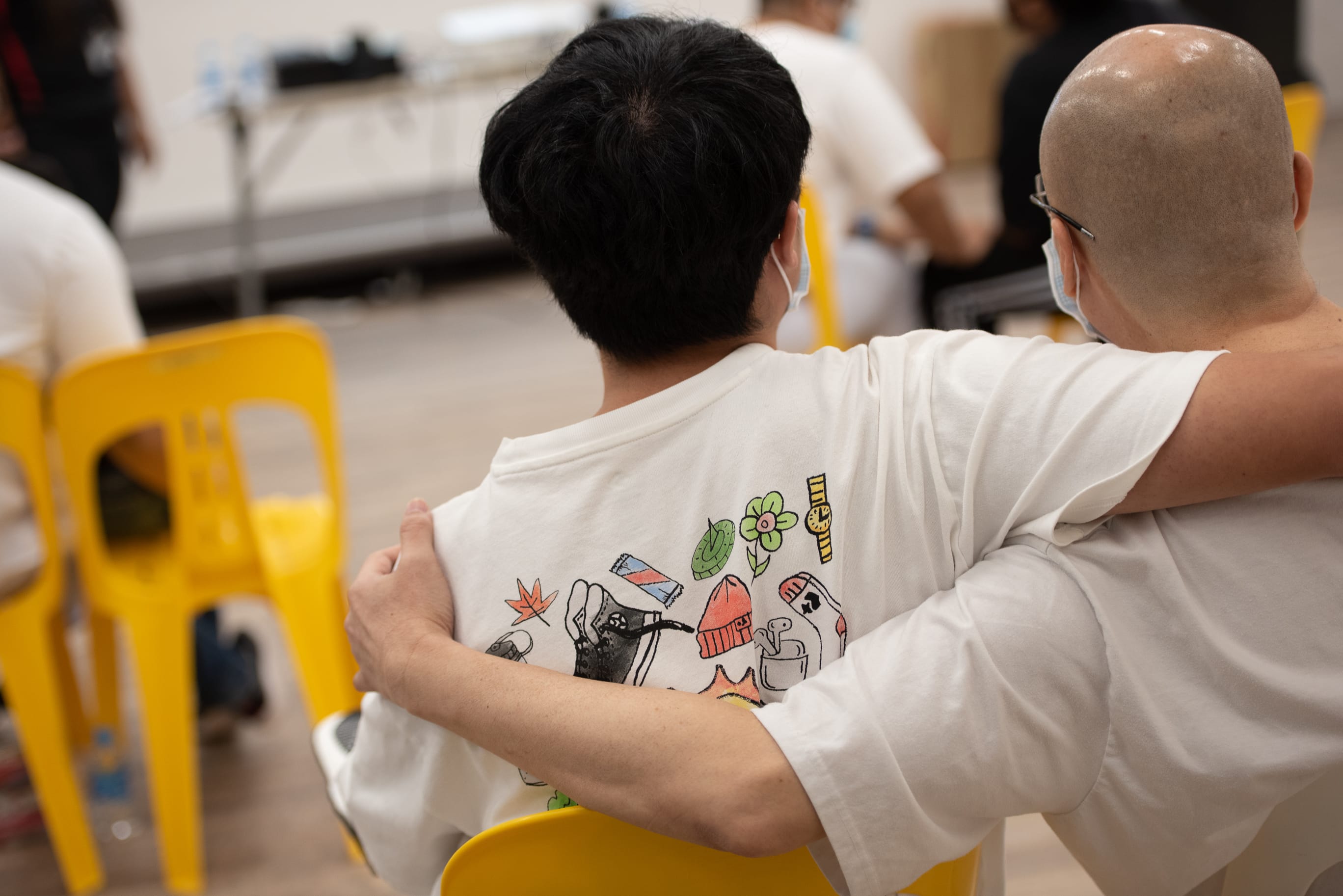 Photo from the backview of an inmate and his family member sitting side-by-side with their arms over the shoulders during a family visit programme in SPS.