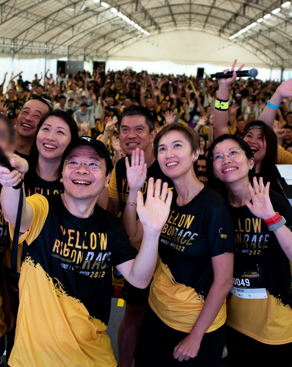 Group in yellow and black shirts cheer on a stage, waving arms, holding horns and a flag.