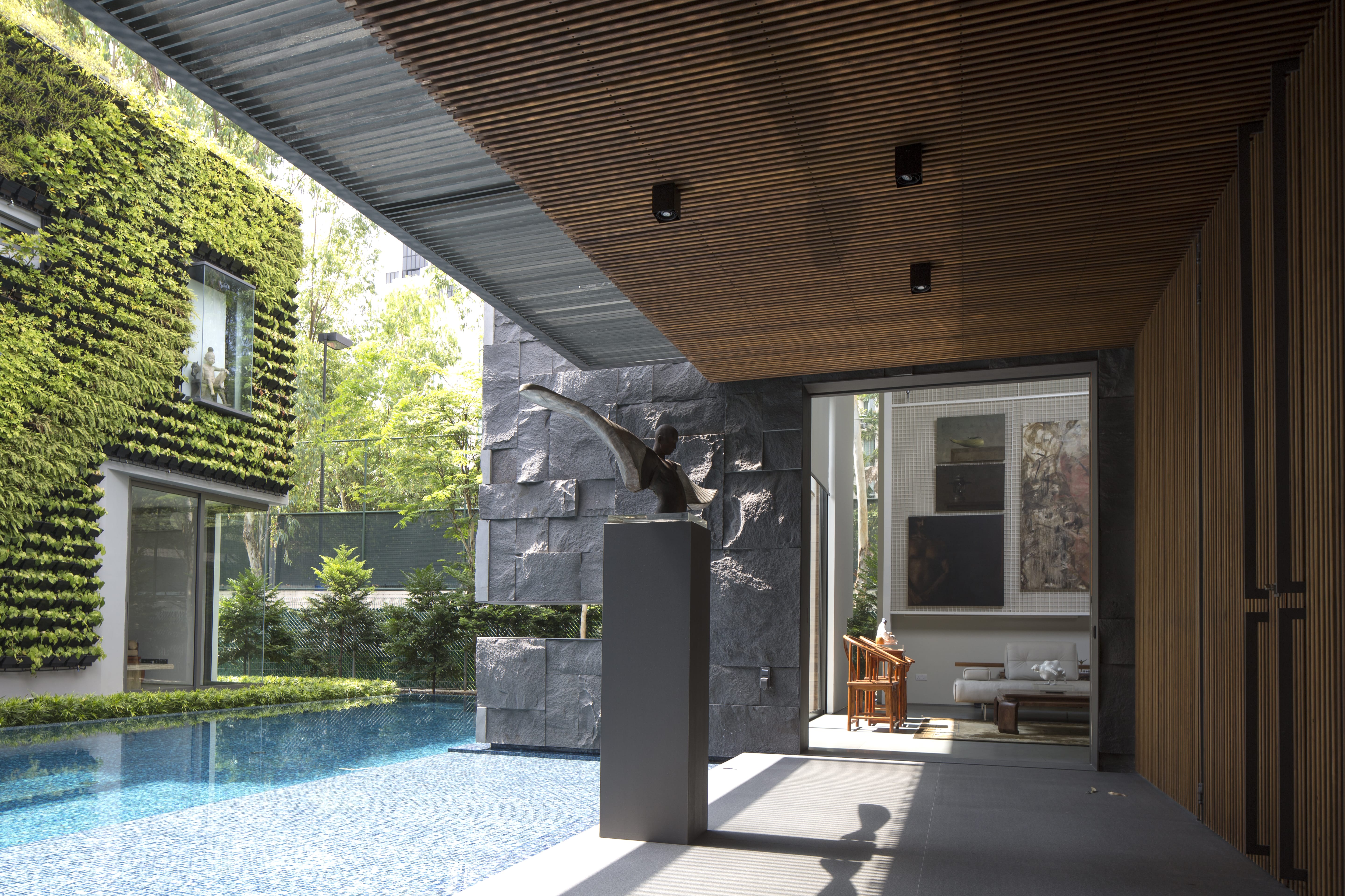 Modern patio with pool, vertical garden, stone wall, and art piece; interior visible through glass door with paintings.