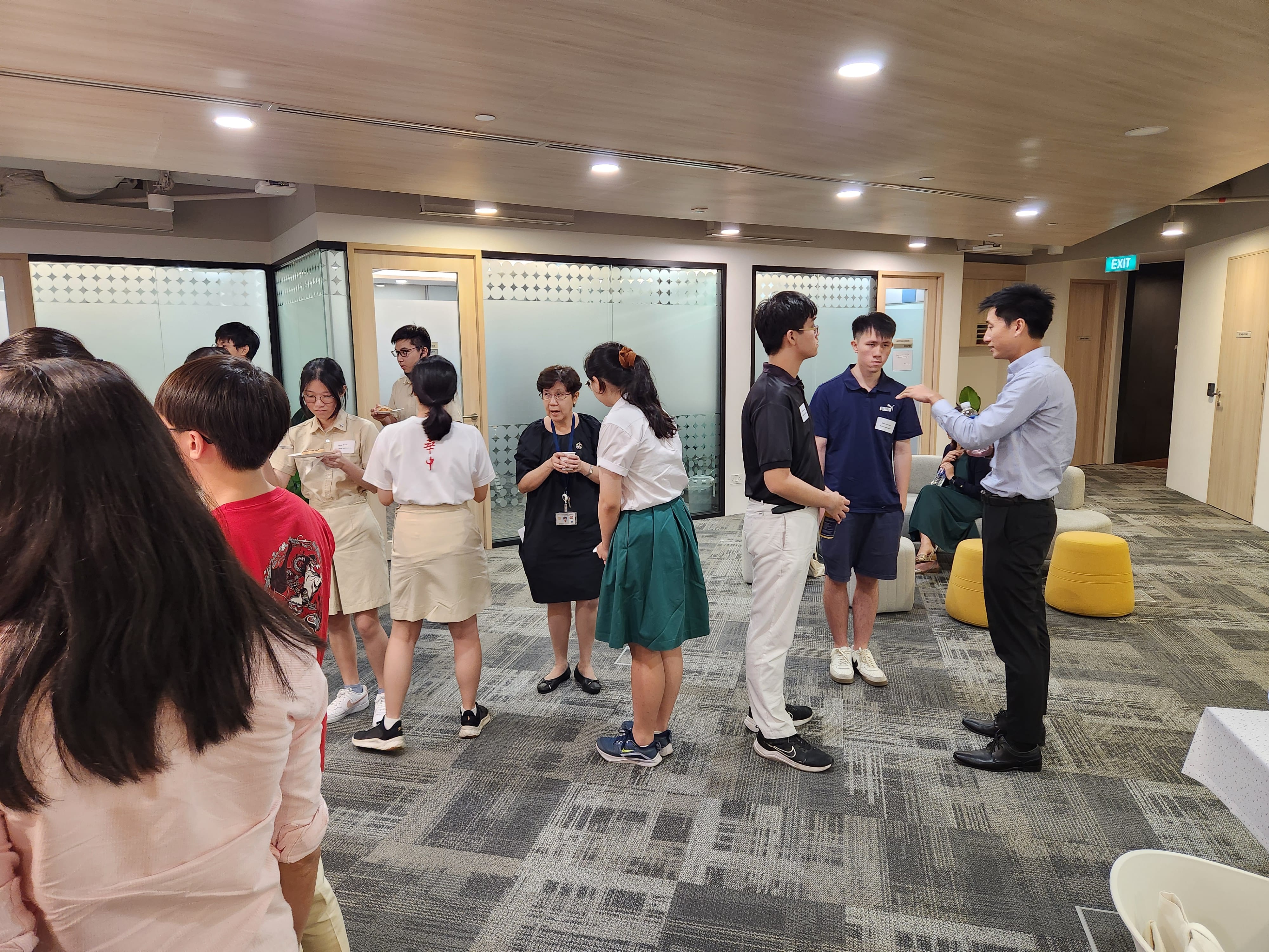 A group of people stands and converses in a modern office lobby with glass walls and furniture.