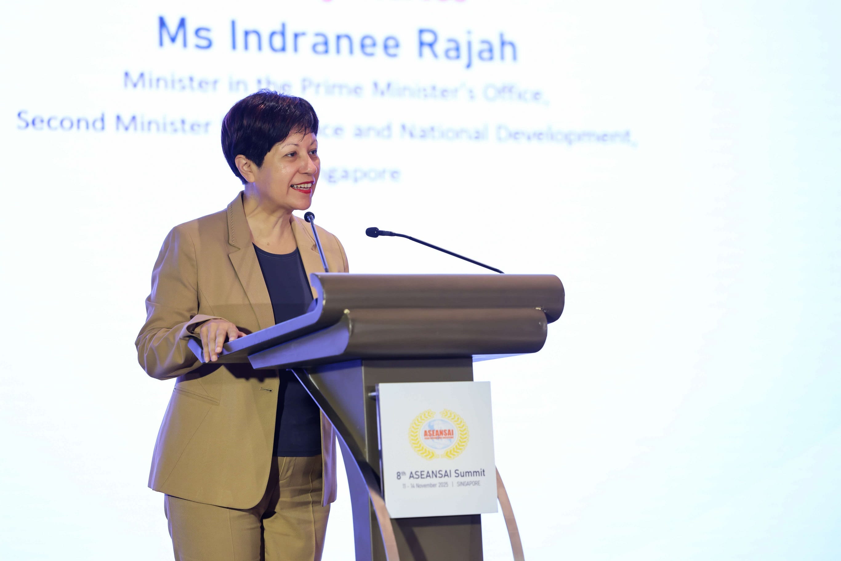A person in a tan suit speaks at a podium displaying the 8th ASEANSAI Summit logo.