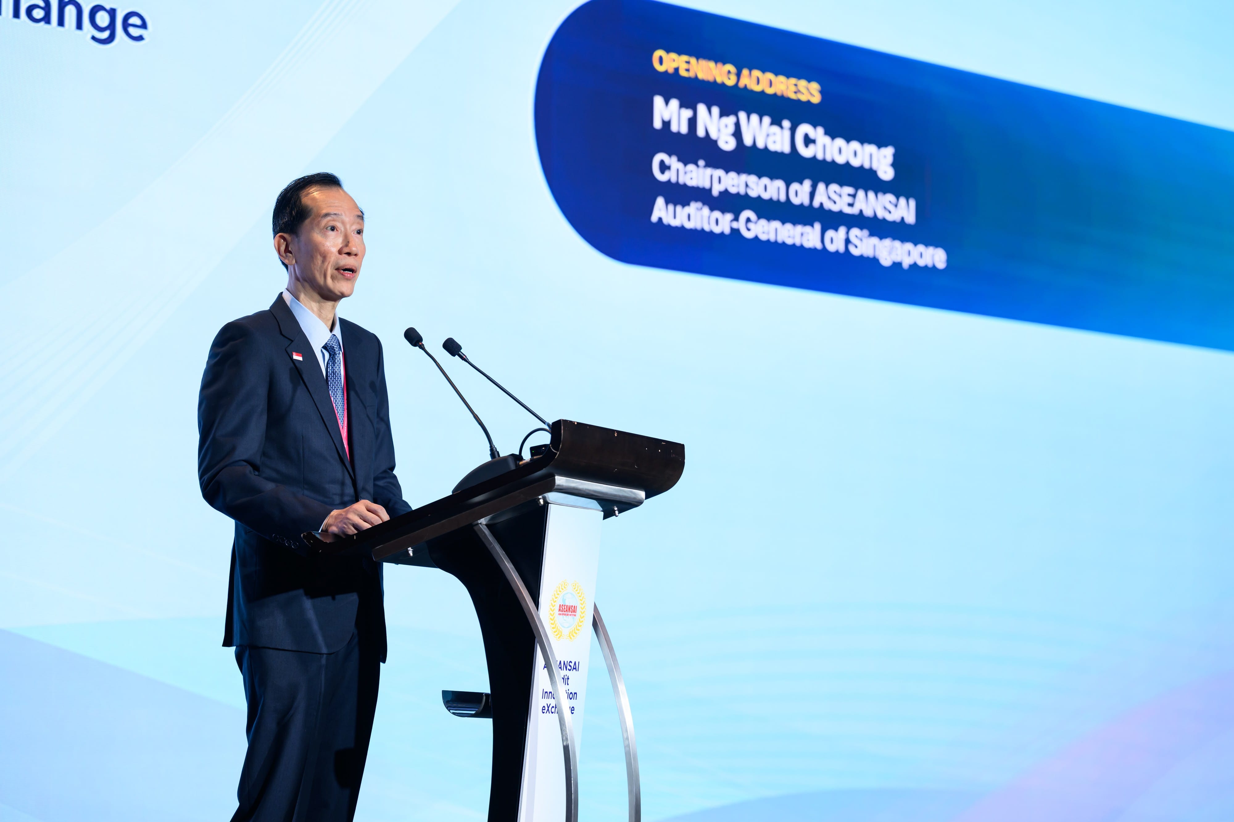 A man speaking at a rostrum, in front of a backdrop that says "Opening Address: Mr Ng Wai Choong, Chairperson of ASEANSAI Auditor-General of Singapore"