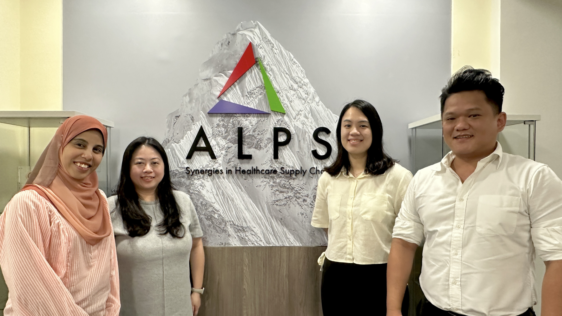 Four people stand in front of an "ALPS" sign with a mountain graphic and the words "Synergies in Healthcare Supply Chain."