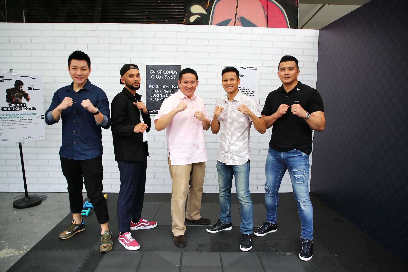 Five people posing with fists up in front of a white brick wall, three posters visible behind them.