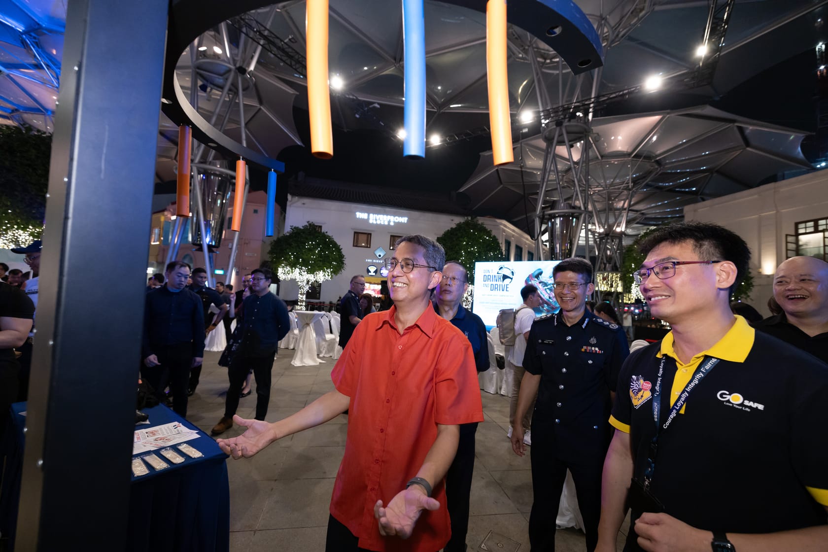 People gathered at an event with decorative lights, a large screen, and an open-air structure above their heads.