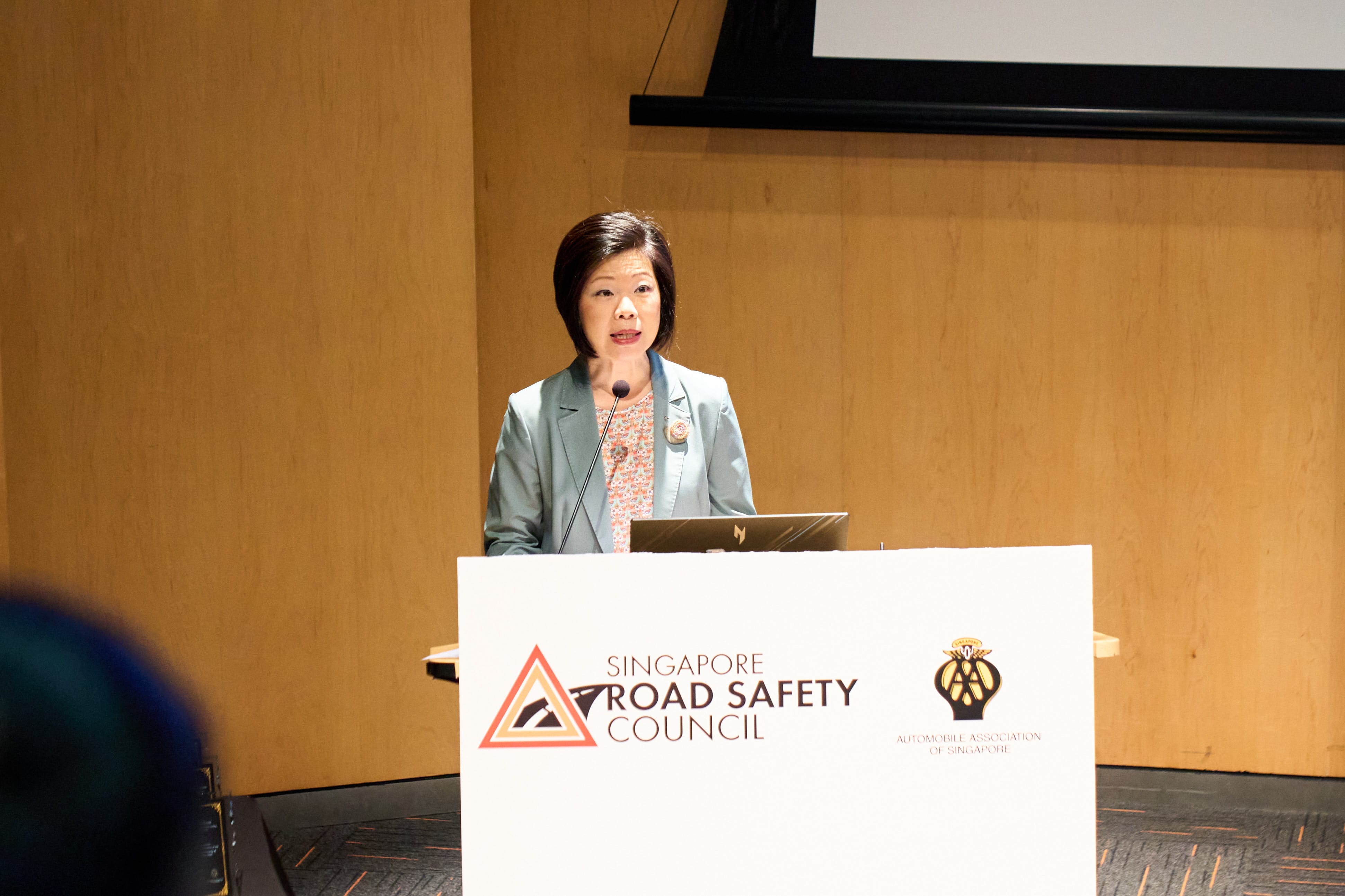 A person stands at a podium with "Singapore Road Safety Council" and "Automobile Association of Singapore" logos.