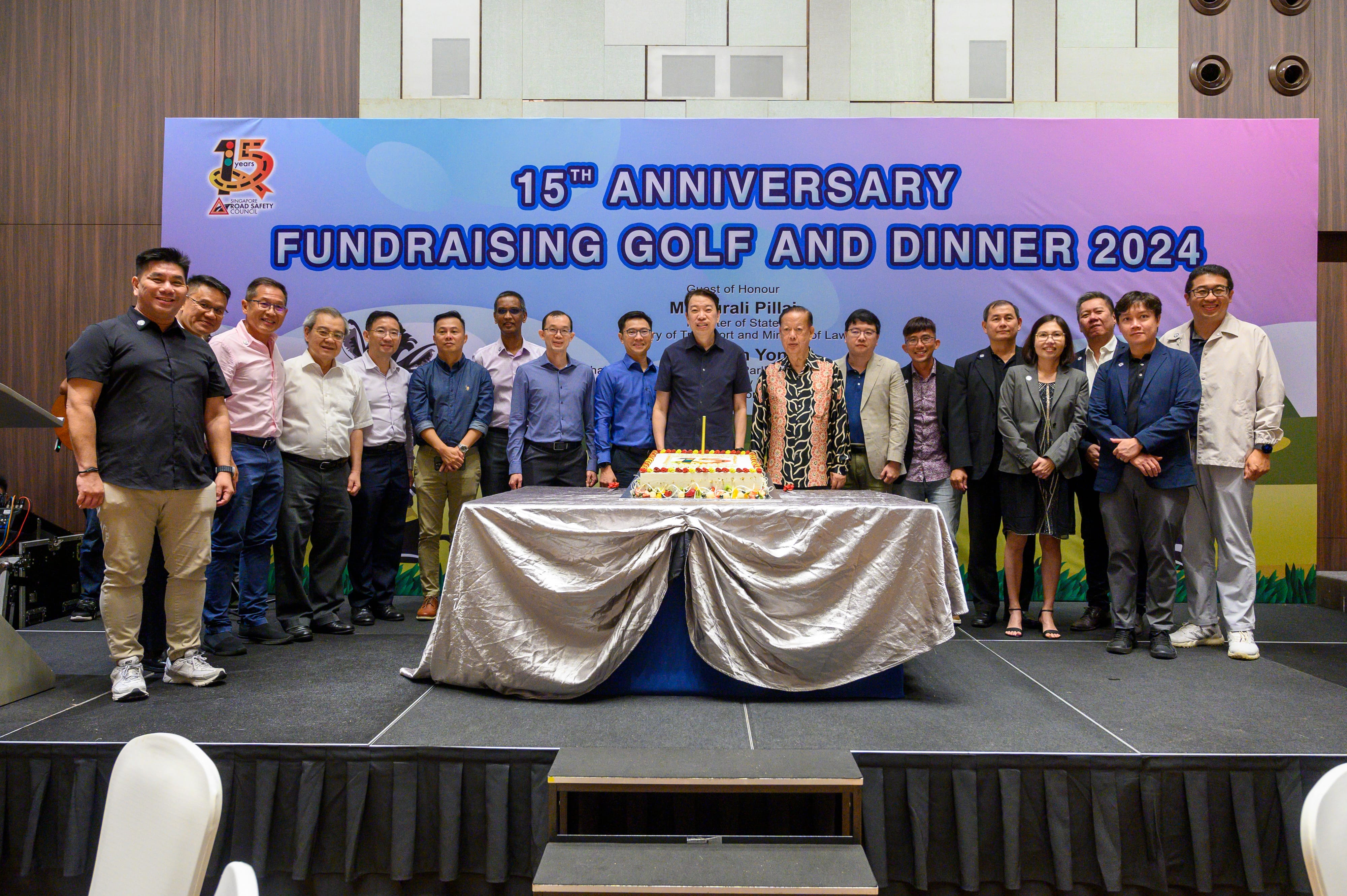A group of people stands on stage behind a cake, under a banner that reads "15th Anniversary Fundraising Golf and Dinner 2024."