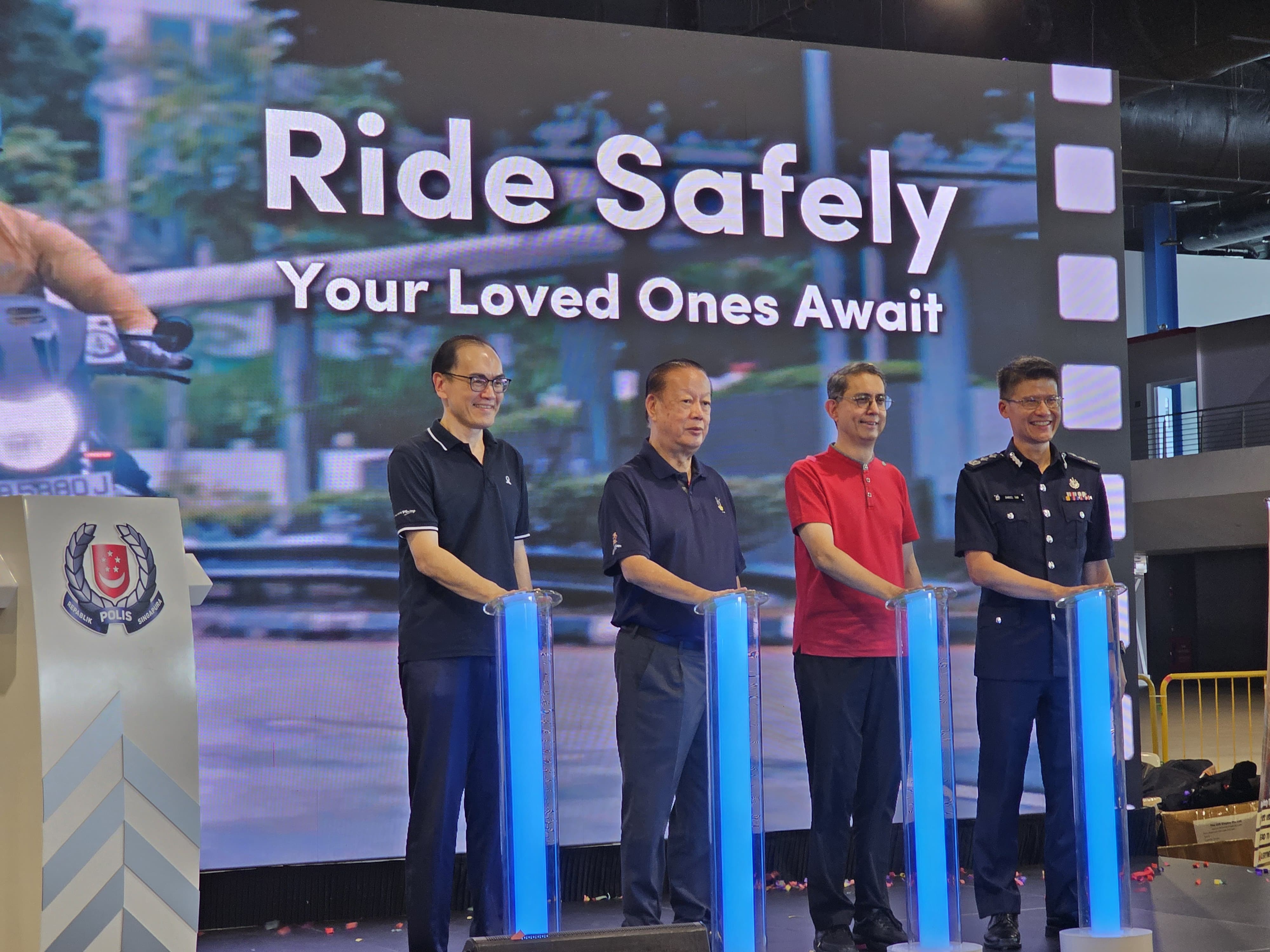 Four individuals stand behind illuminated podiums in front of a "Ride Safely, Your Loved Ones Await" sign.