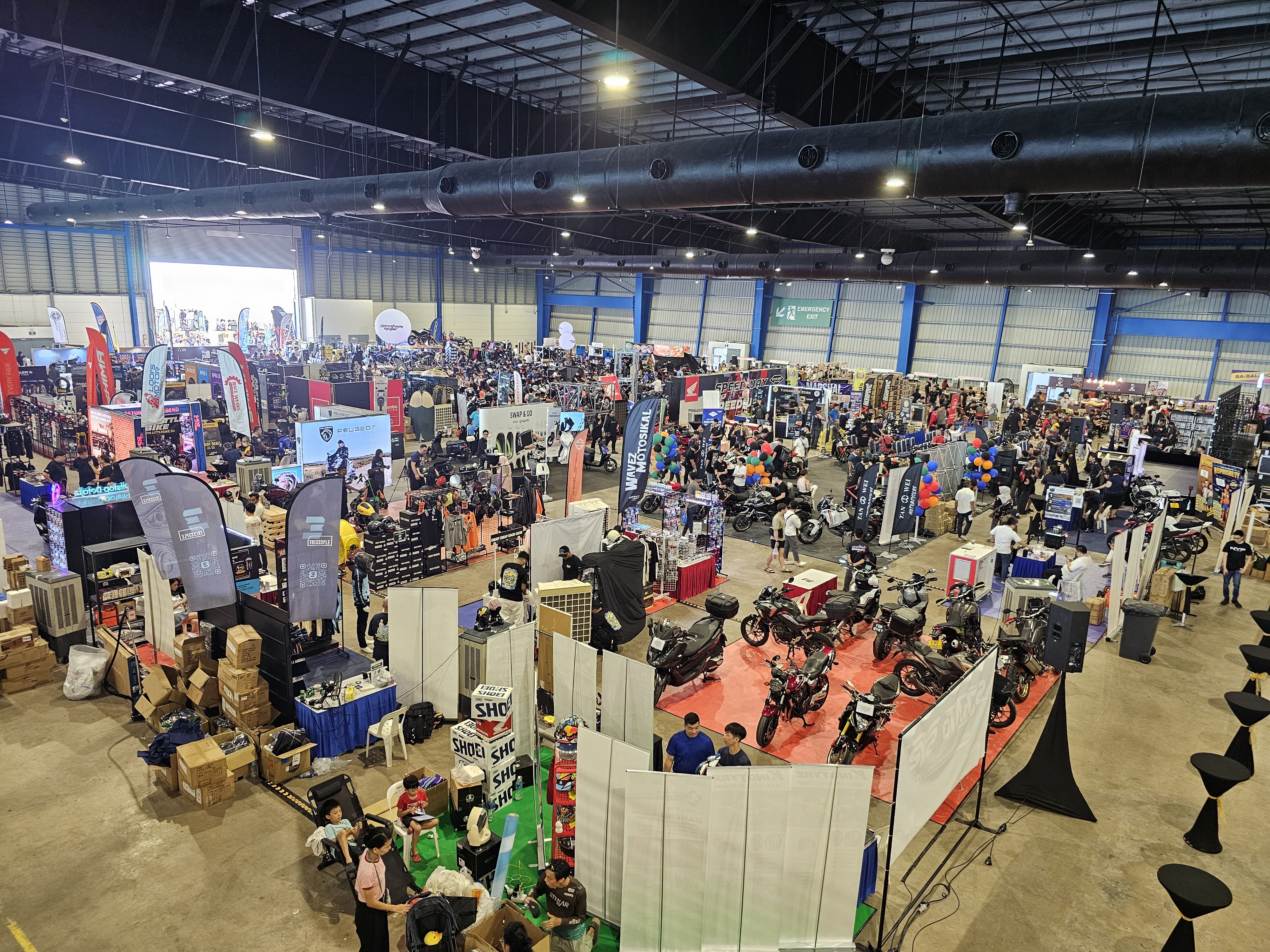 Large indoor exhibition with booths, motorcycles, banners, and people walking around.