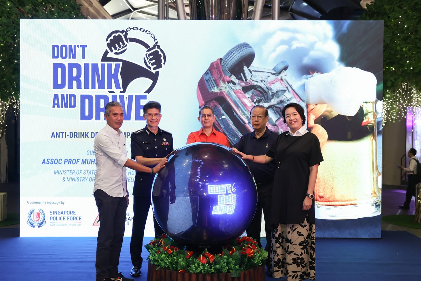 Four people stand around a large globe with "Don't Drink and Drive" text in front of a banner showing a crashed car and beer.